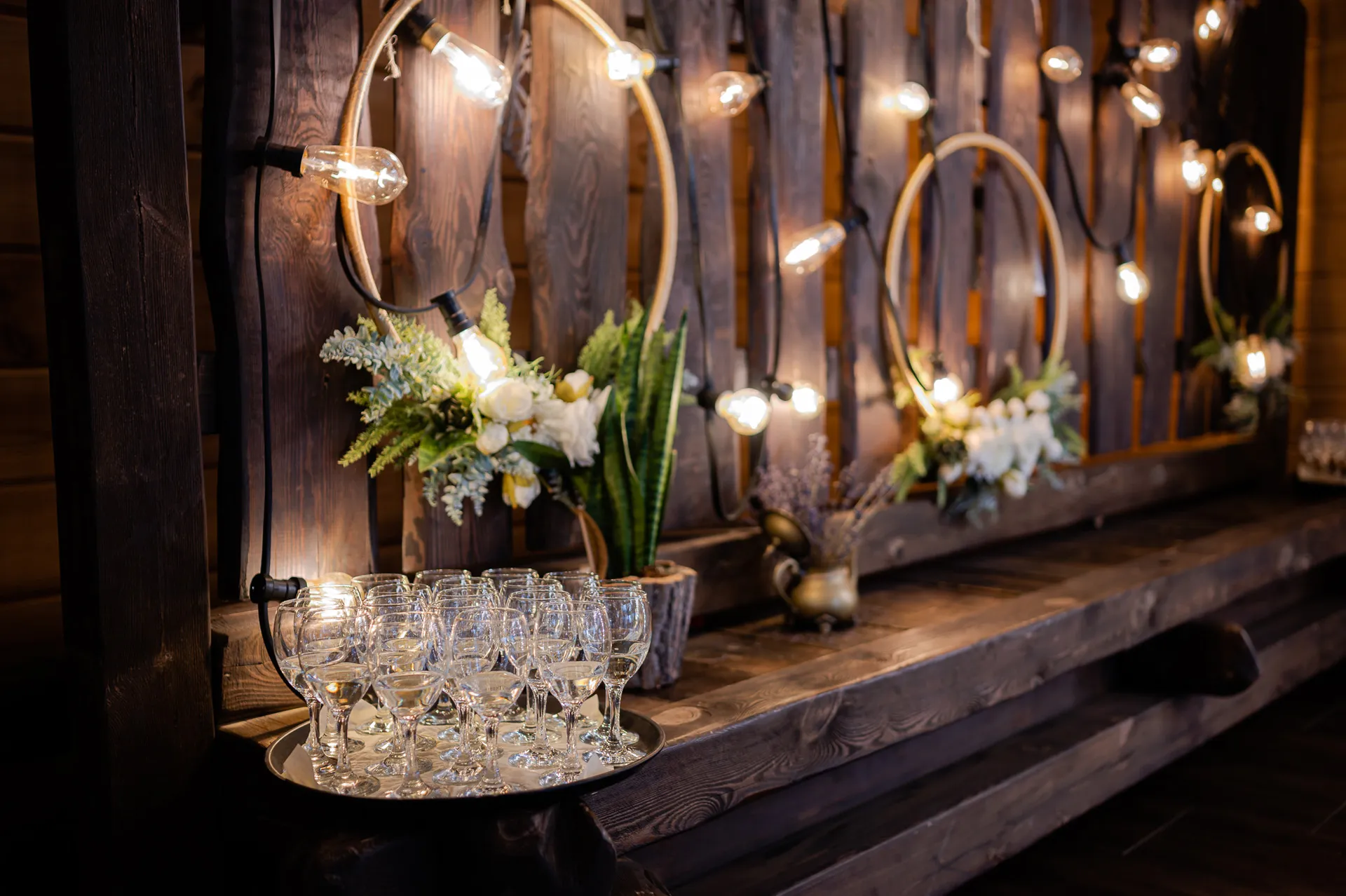 Elegancki bar weselny z lampkami Edison, kieliszkami wina i dekoracjami kwiatowymi, rustykalny styl ślubu
