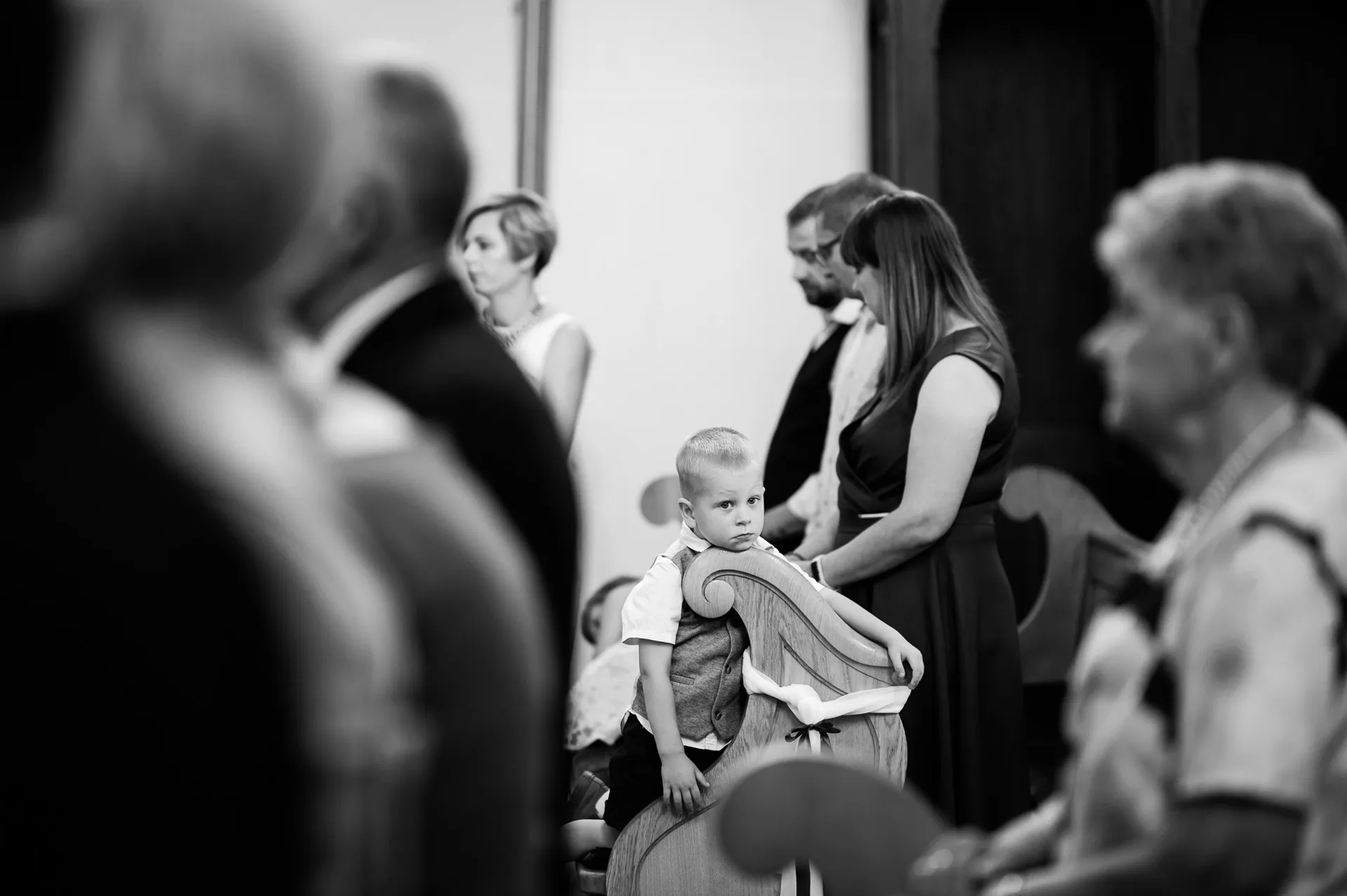 Czarno-białe zdjęcie gości weselnych w kościele podczas ceremonii - małe dziecko siedzi spokojnie wśród dorosłych gości w eleganckich strojach