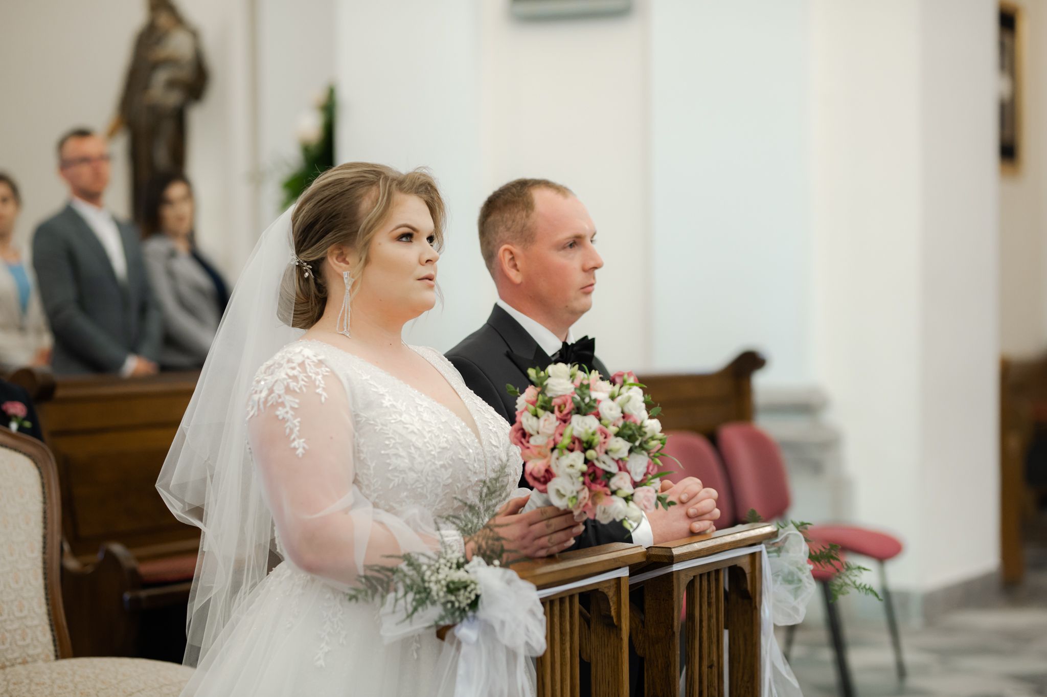 Ceremonia ślubna w kościele - para młoda stoi przy ołtarzu podczas przysięgi małżeńskiej, panna młoda w koronkowej sukni z bukietem, pan młody w czarnym garniturze
