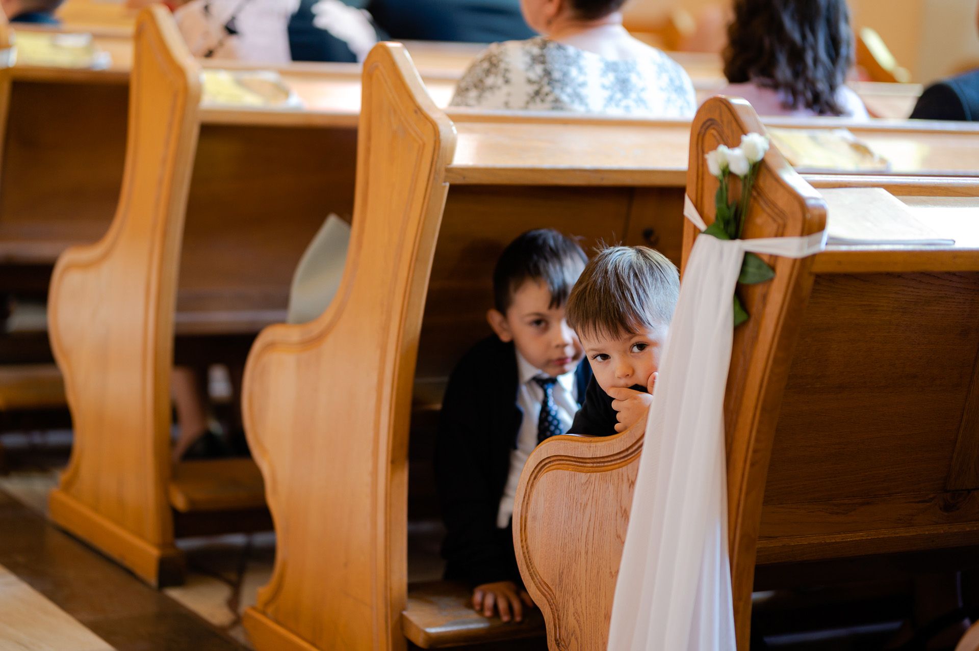 Dzieci uczestniczące w ceremonii ślubnej siedzą w ławkach kościelnych - chłopiec i dziewczynka w eleganckich strojach podczas uroczystości