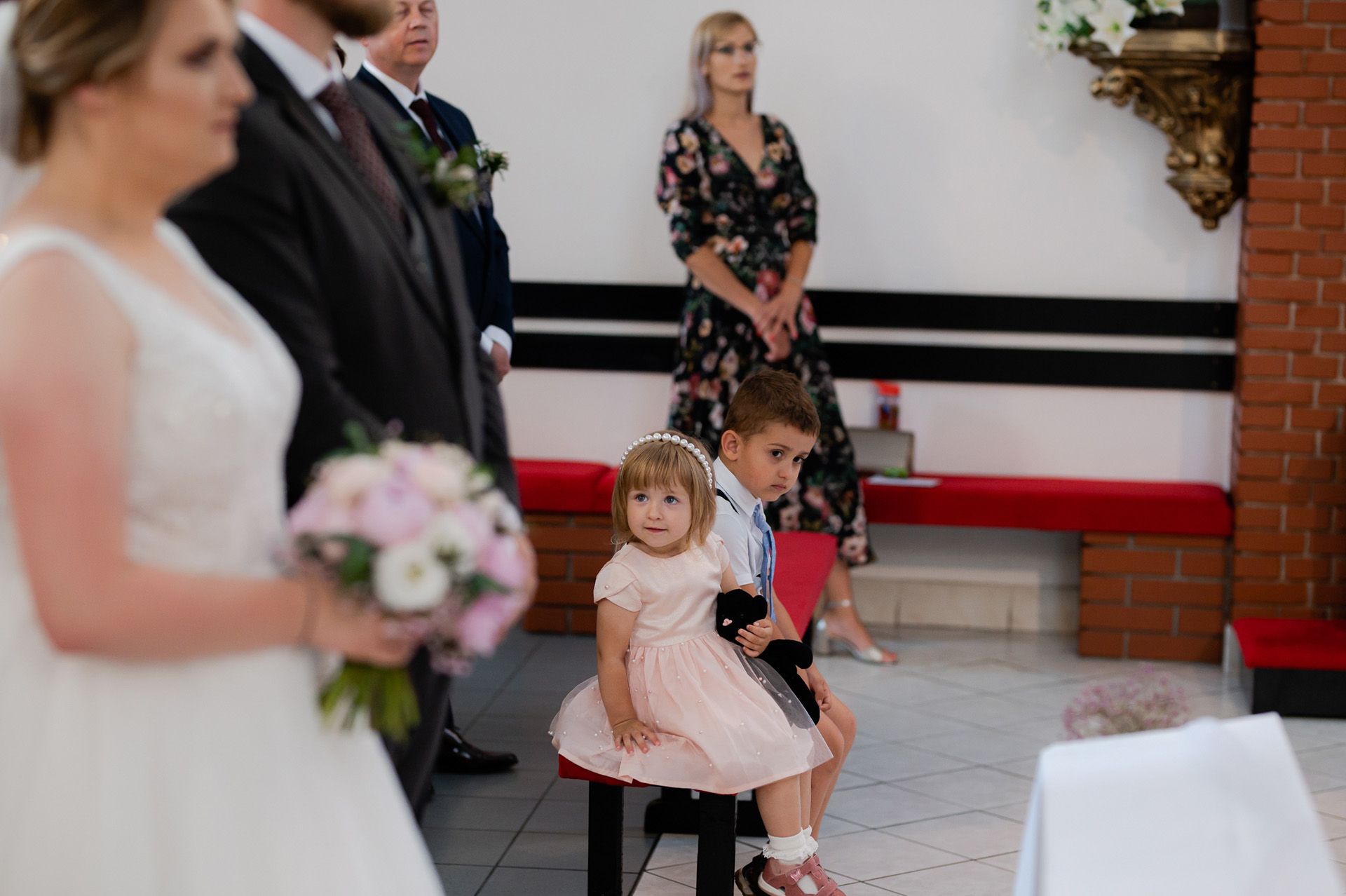 Dzieci w eleganckich strojach podczas ślubu - dziewczynka w różowej sukience i chłopiec w garniturze siedzą podczas ceremonii