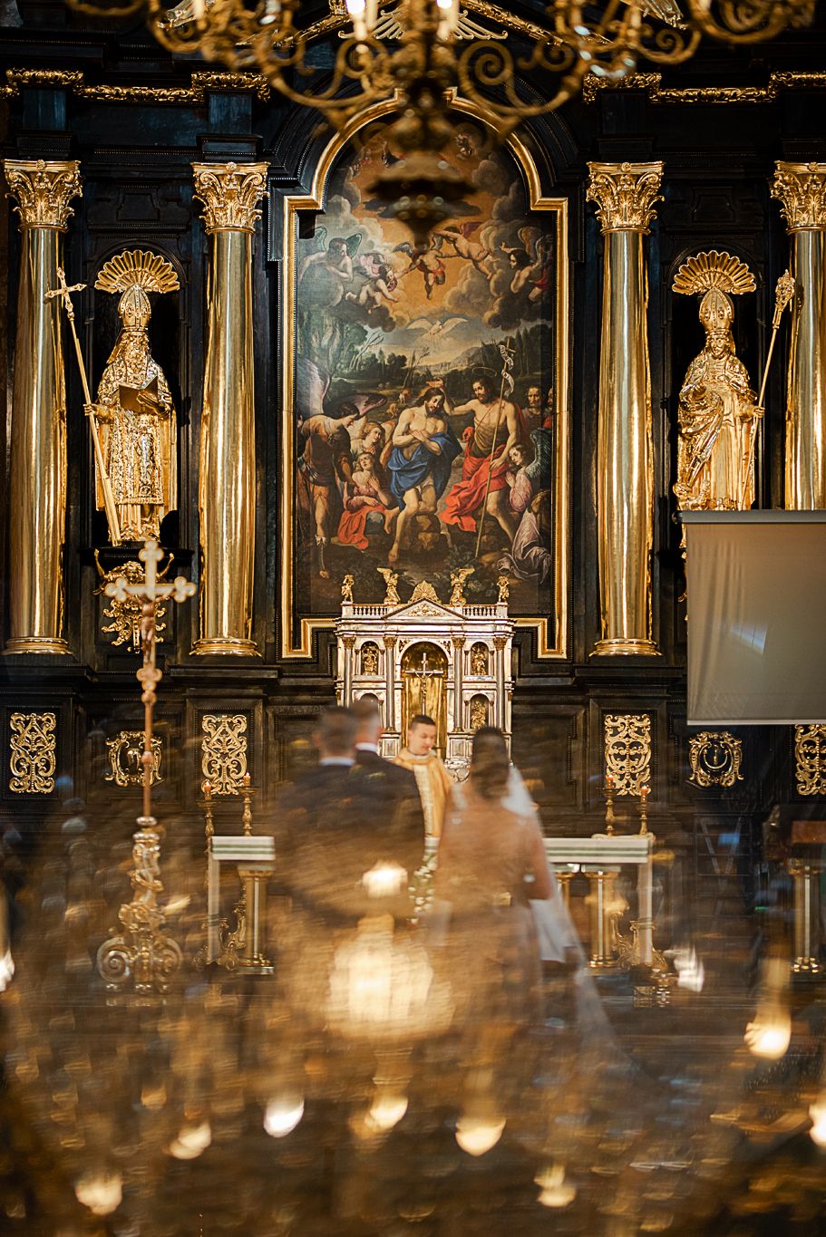 Bogato zdobiony ołtarz kościelny ze złotymi elementami i religijnymi obrazami, para młoda podczas ceremonii ślubnej w sakralnym wnętrzu