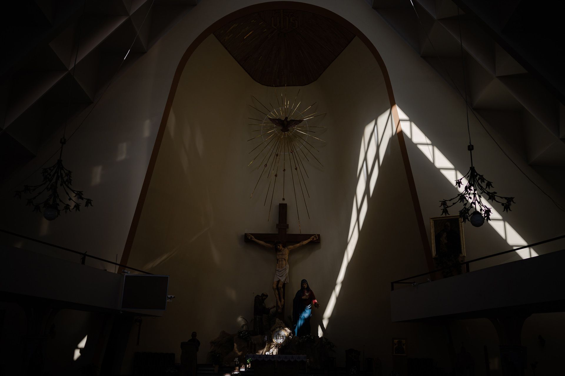 Wnętrze kościoła z krzyżem i figurą Matki Boskiej, dramatyczne światło słoneczne podczas ceremonii ślubnej, sakralna atmosfera