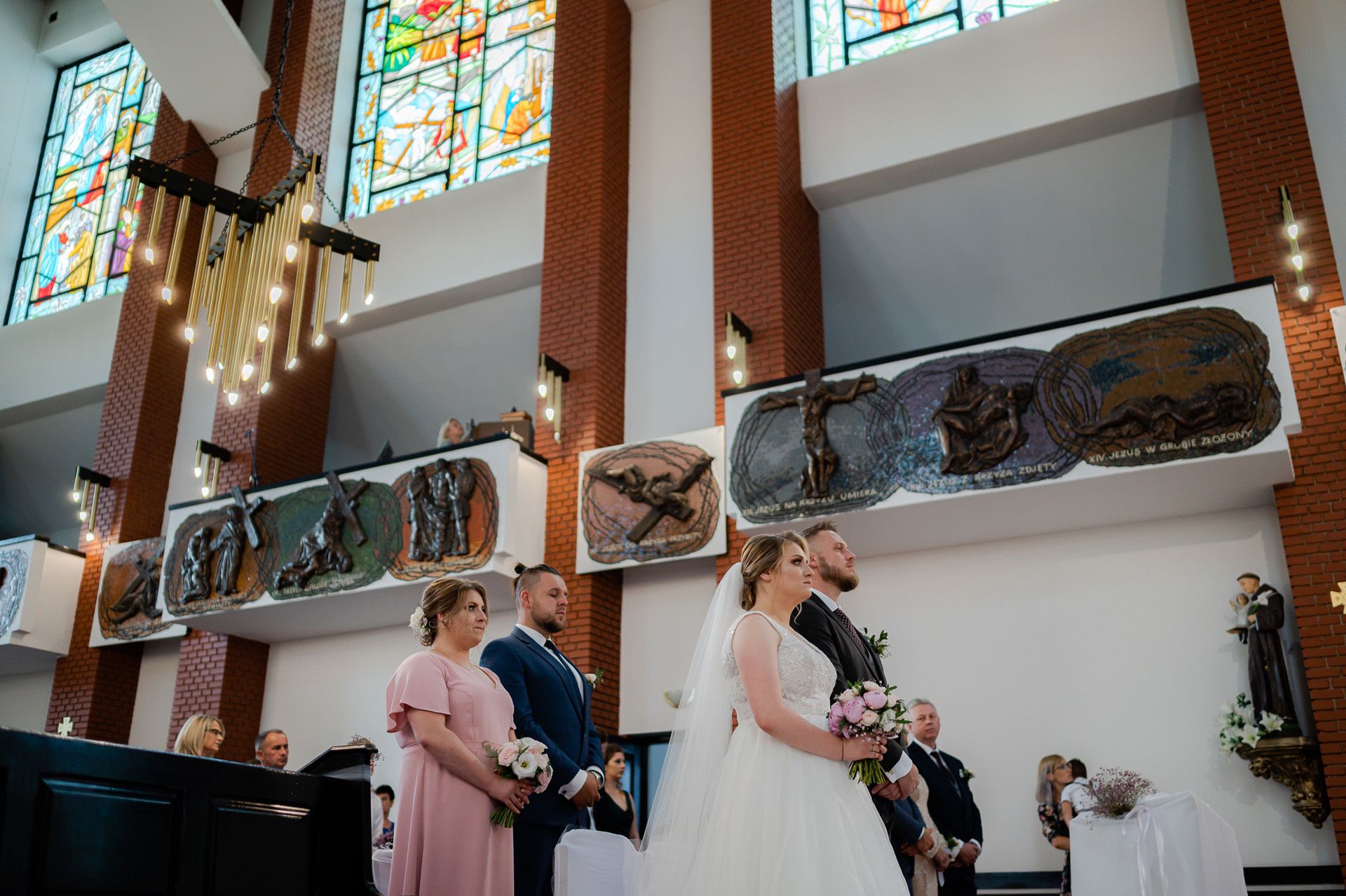 Ceremonia ślubna w nowoczesnym kościele z kolorowymi witrażami, para młoda przy ołtarzu z druhną w różowej sukni