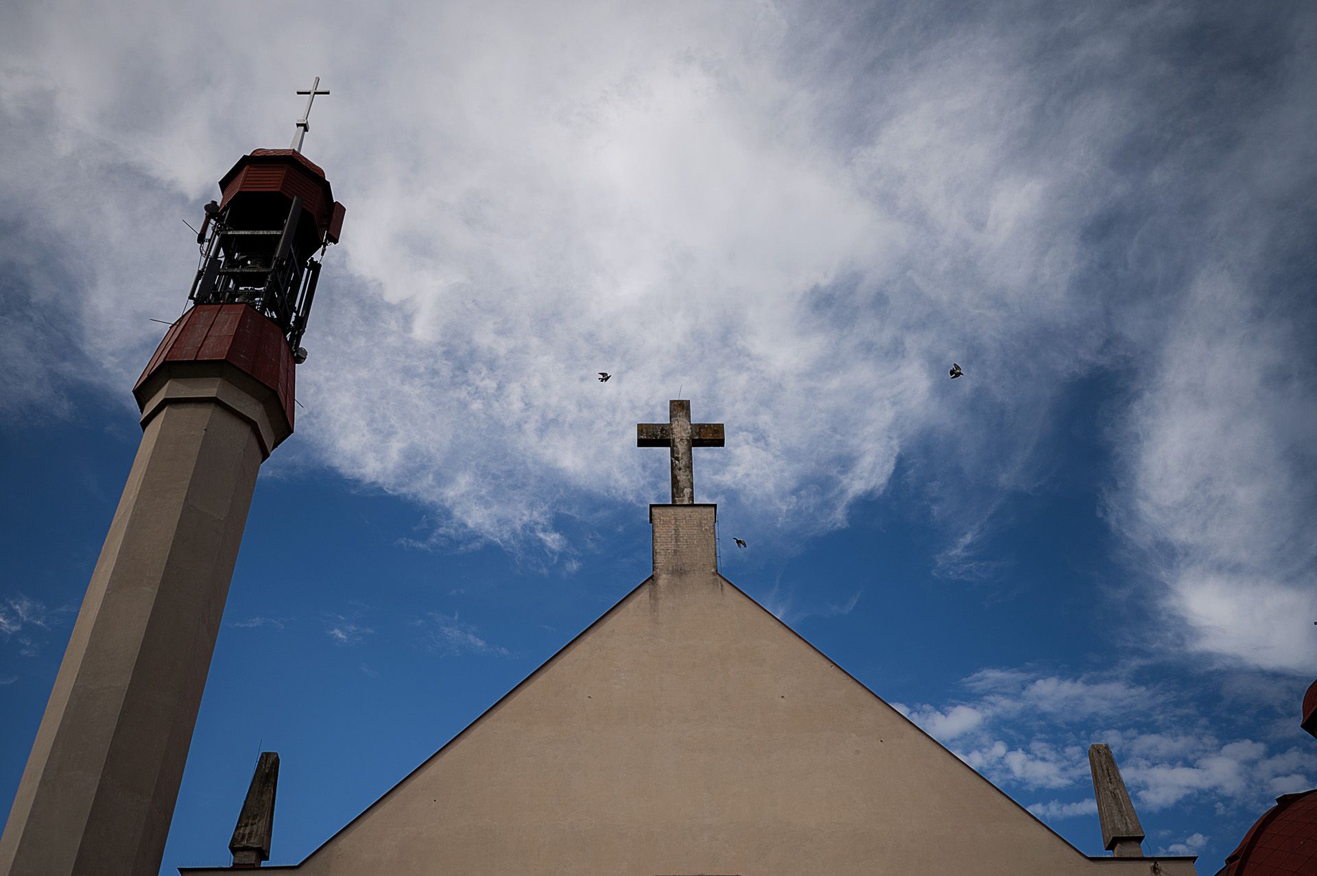 Wieża kościoła z krzyżem na tle błękitnego nieba z chmurami podczas uroczystości ślubnej, architektura sakralna