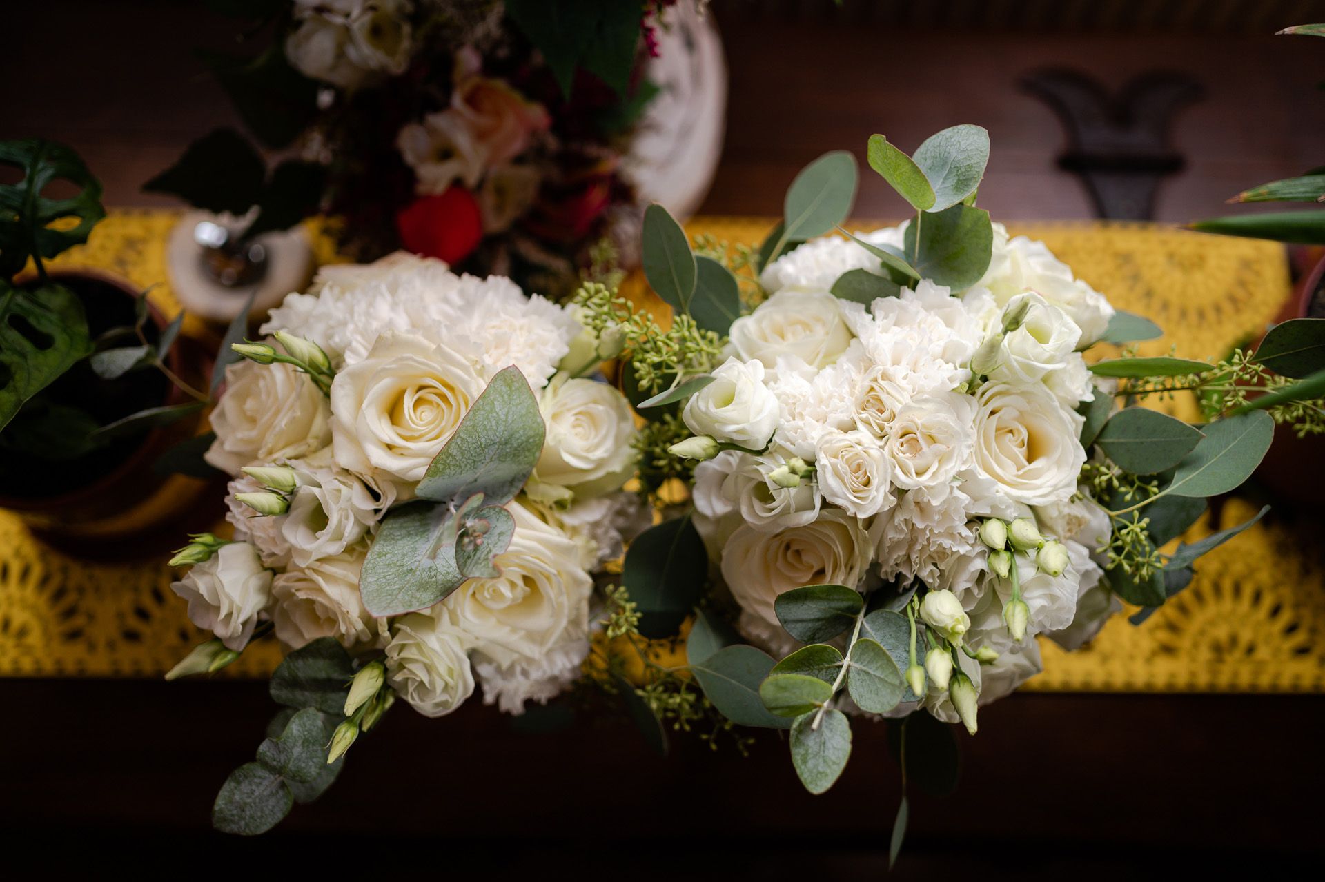 Dwa białe bukiety ślubne z róż, eustomy i eukaliptusa ułożone na żółtym materiale