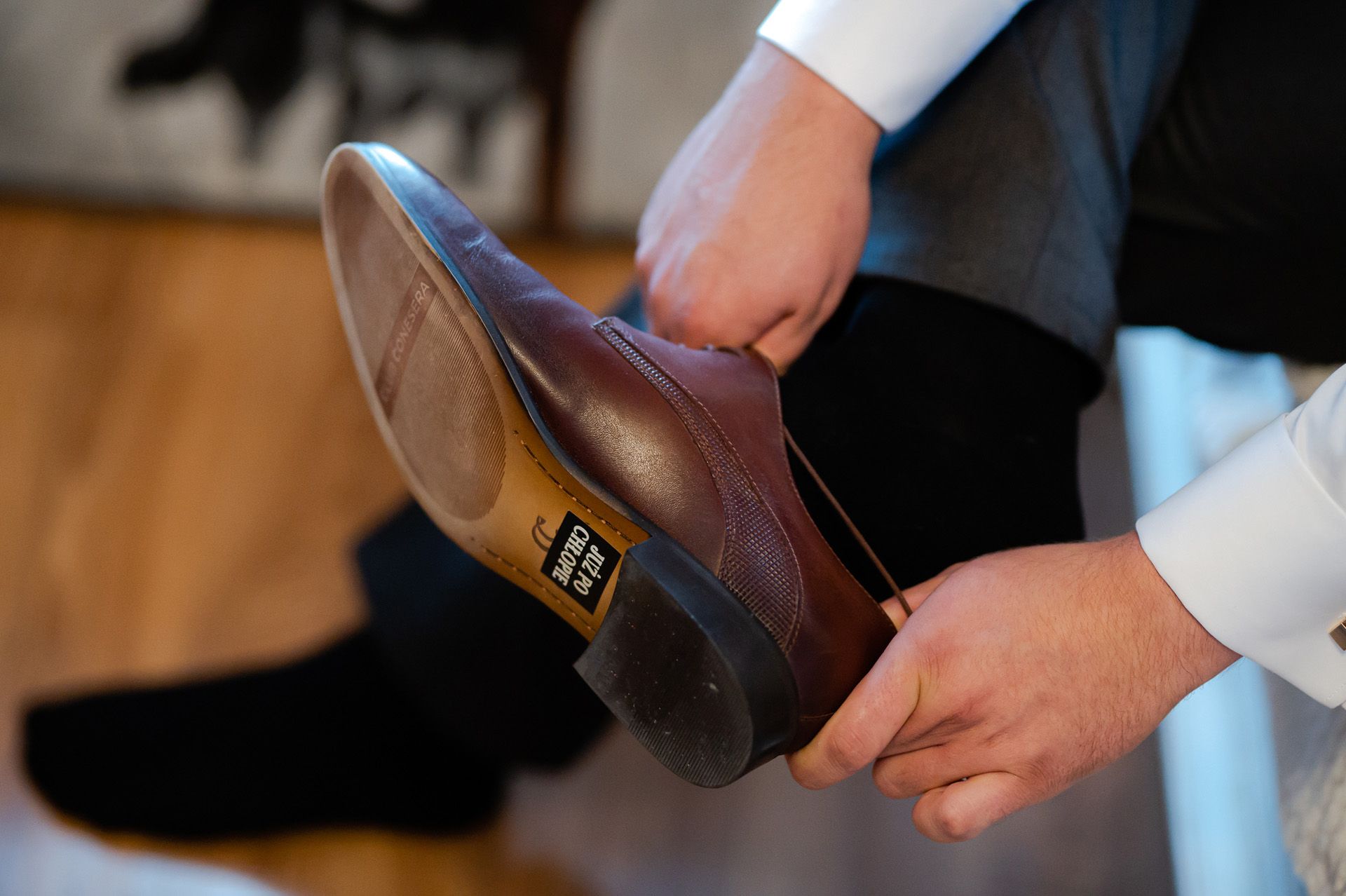 Mężczyzna w białej koszuli trzymający eleganckie brązowe buty ślubne ze skóry