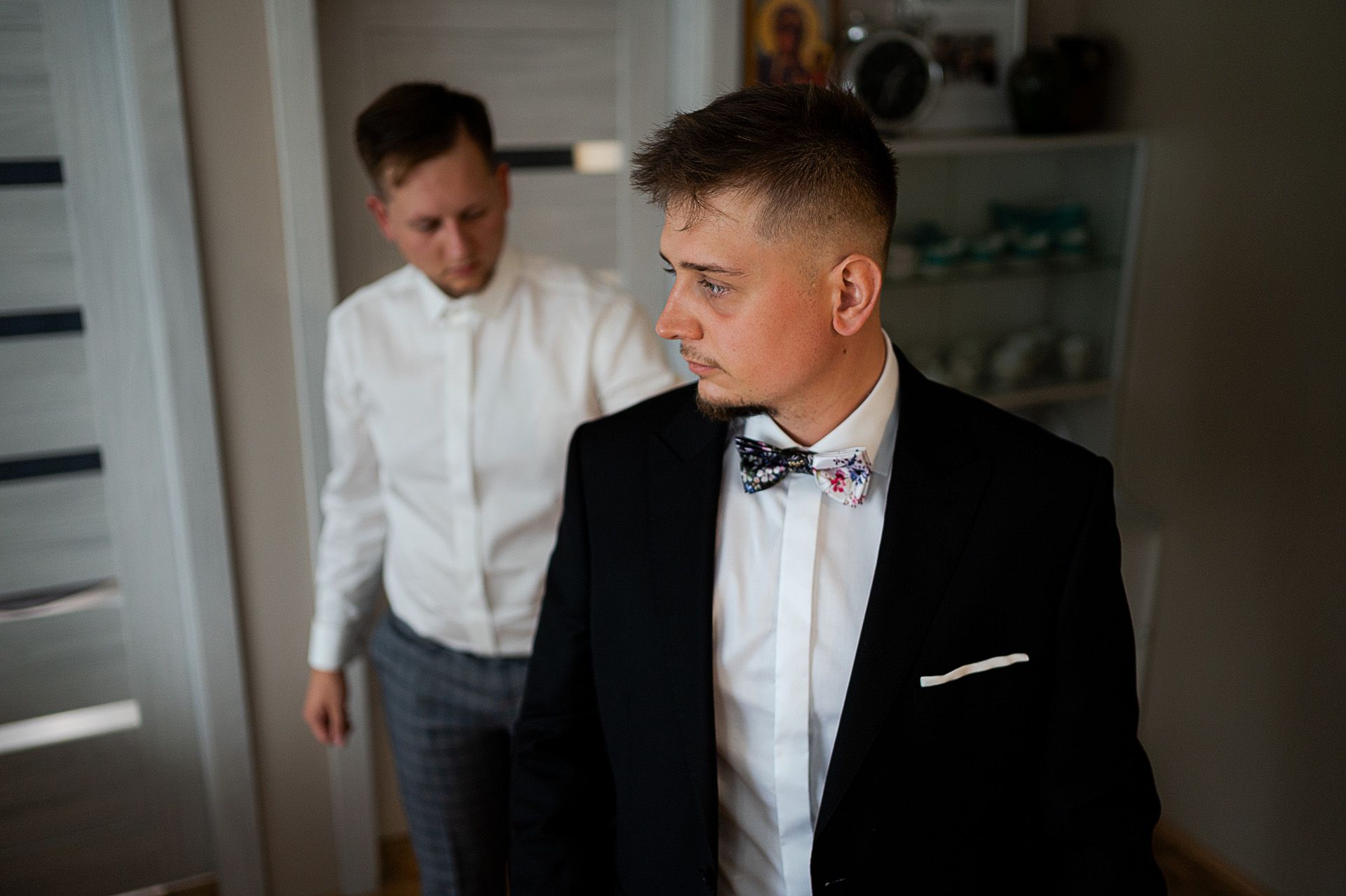 Pan młody w czarnym garniturze z kwiecistą muchą podczas przygotowań ślubnych w domu