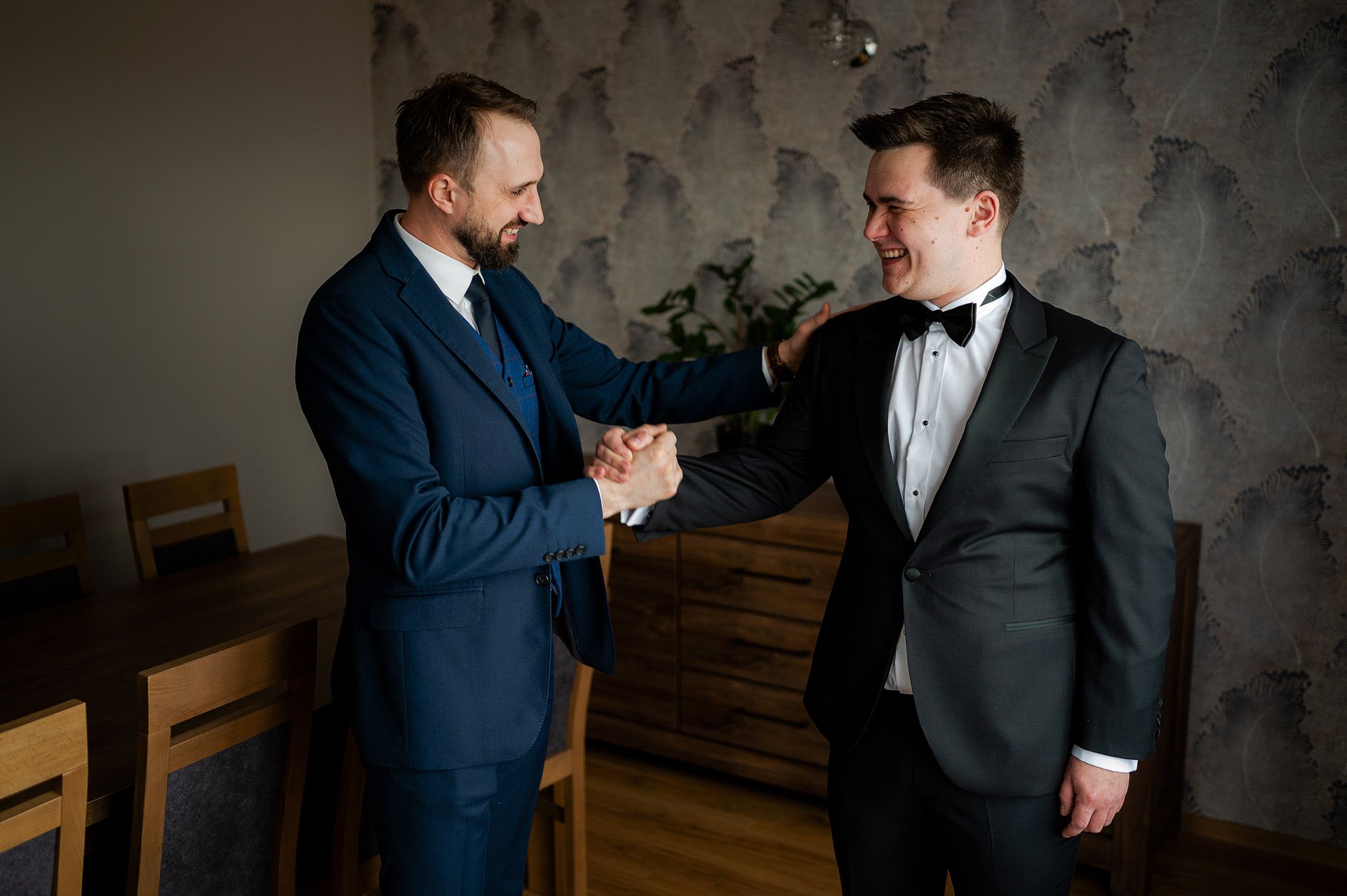 Pan młody w niebieskiej marynarce ściskający dłoń drugiej osoby w czarnym garniturze