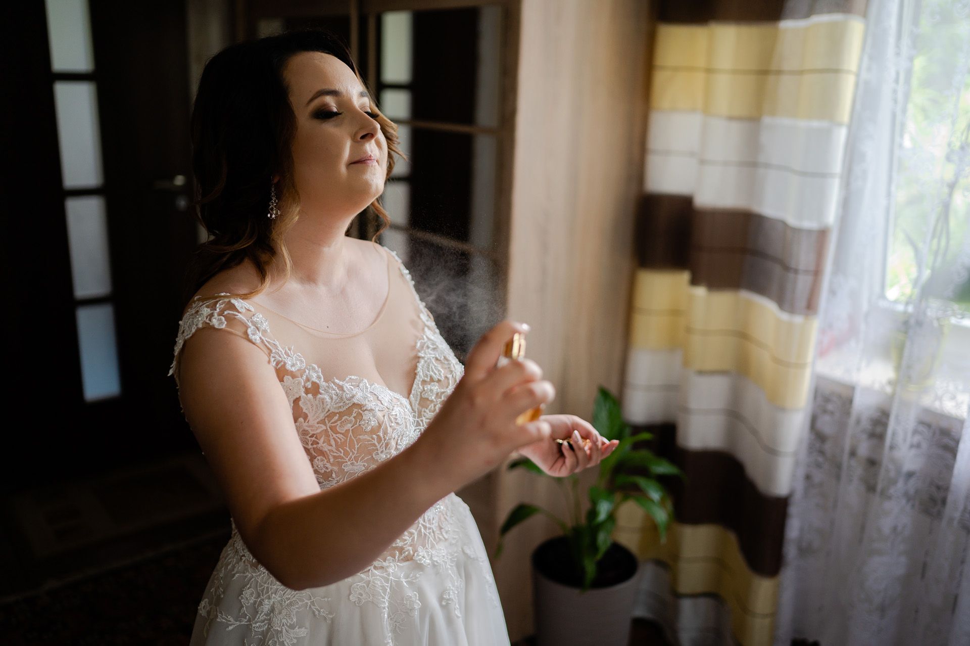 Panna młoda w białej koronkowej sukni ślubnej rozpylająca perfumy w pomieszczeniu