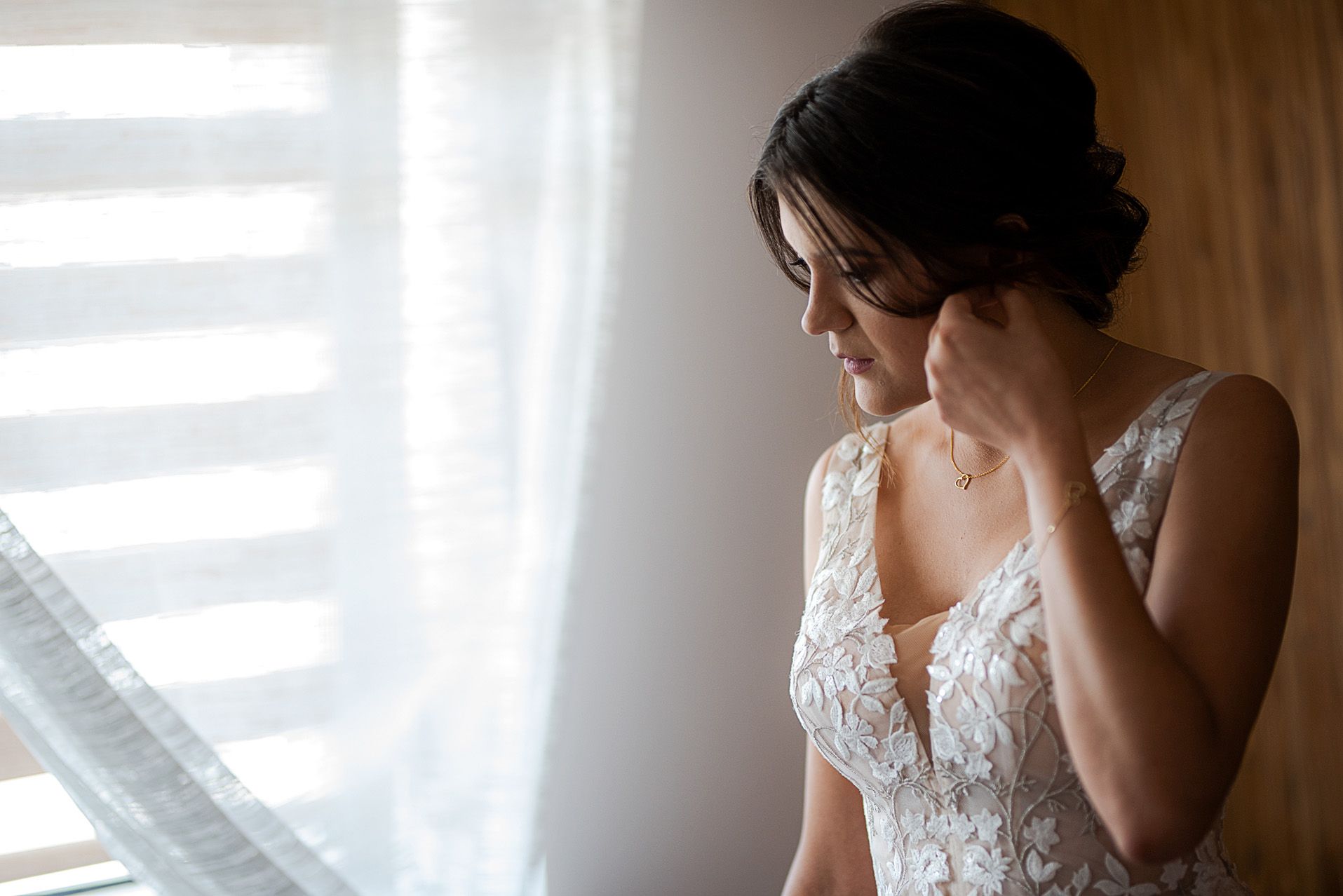 Panna młoda w koronkowej sukni ślubnej pozująca przy oknie w naturalnym świetle