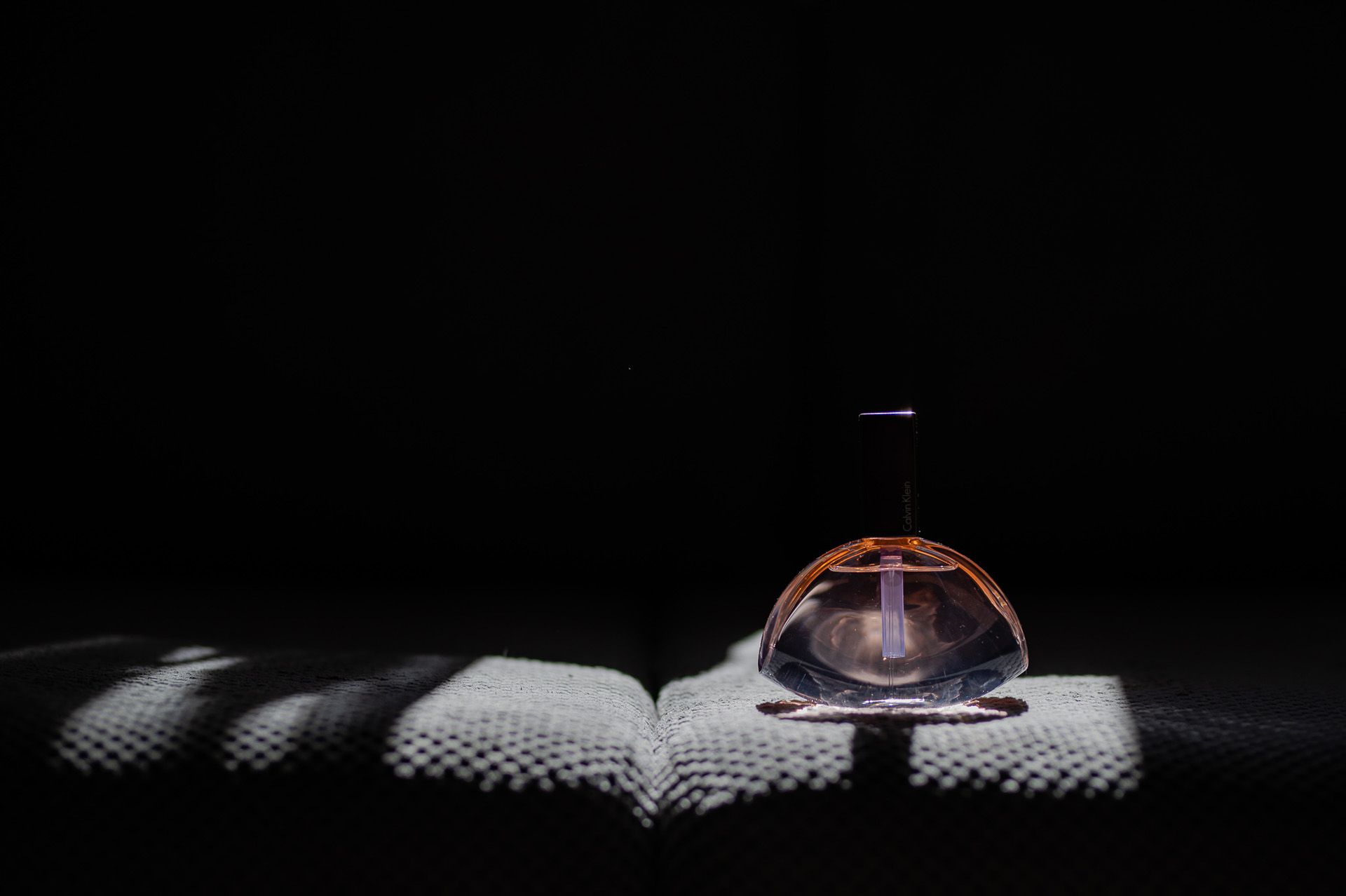 Elegancka butelka perfum na białej tkaninie z dramatycznym oświetleniem na czarnym tle
