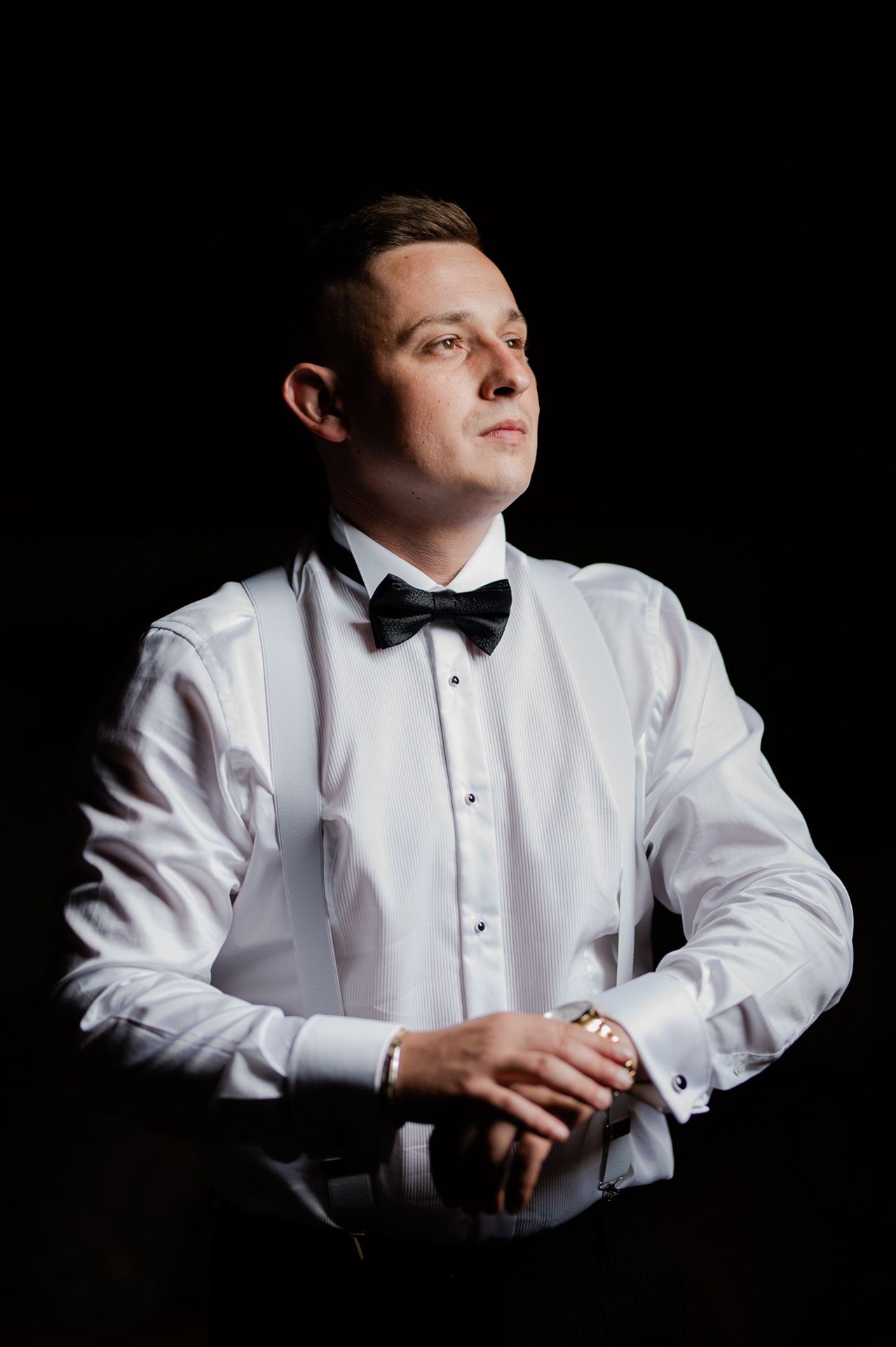 Elegancki portret pana młodego w białej koszuli z plisami i czarnej muszce na ciemnym tle