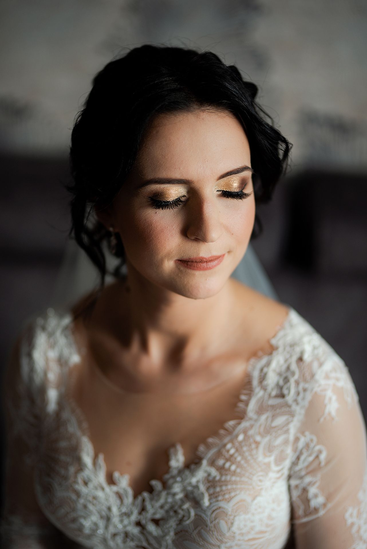 Artystyczny portret panny młodej z zamkniętymi oczami i złotym makijażem w koronkowej sukni