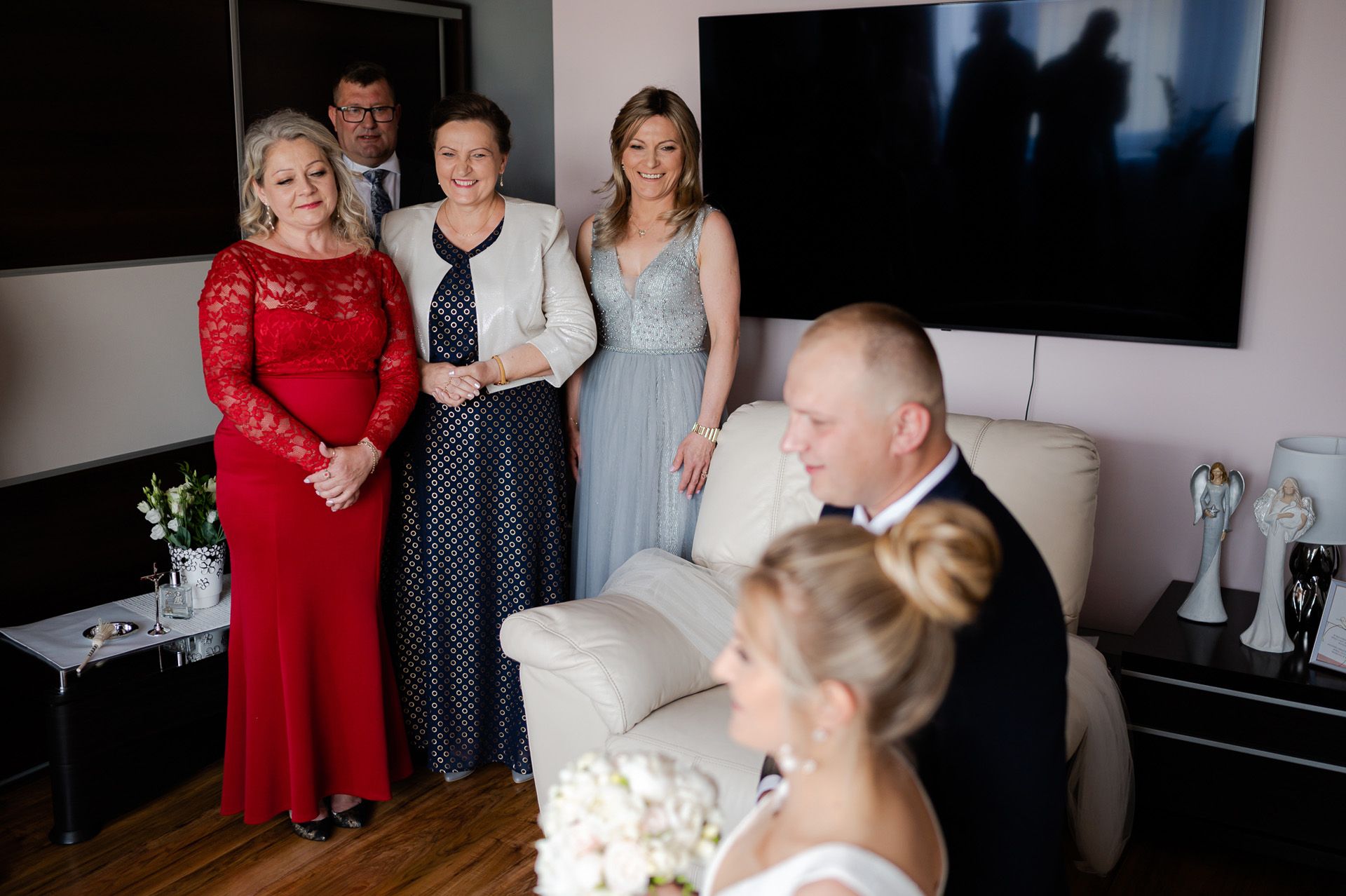 Elegancko ubrani goście weselni w salonie - kobiety w czerwonych i niebieskich sukniach, mężczyźni w garniturach