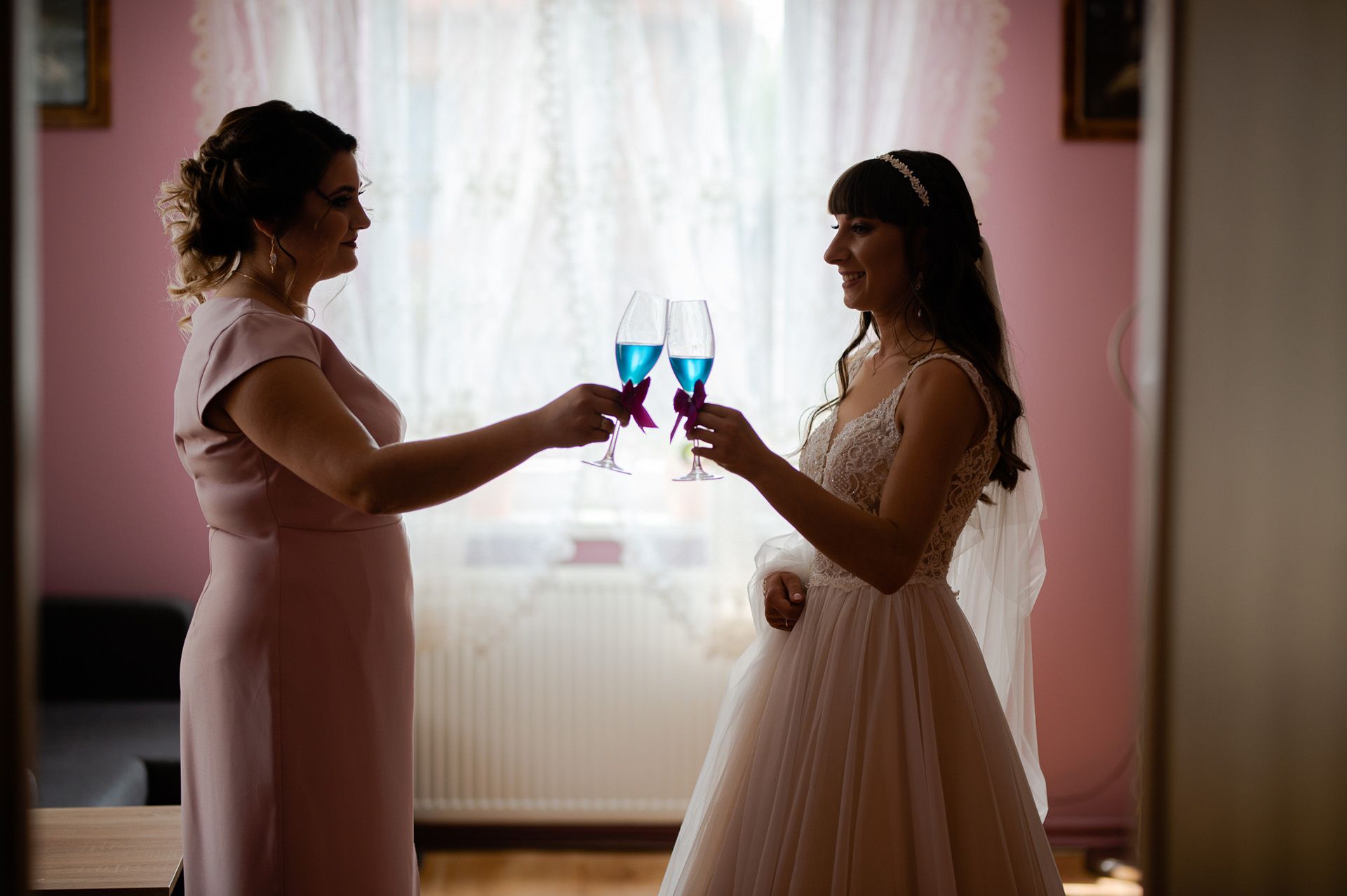 Panna młoda w koronkowej sukni wznoszącą toast niebieskimi drinkami z inną kobietą