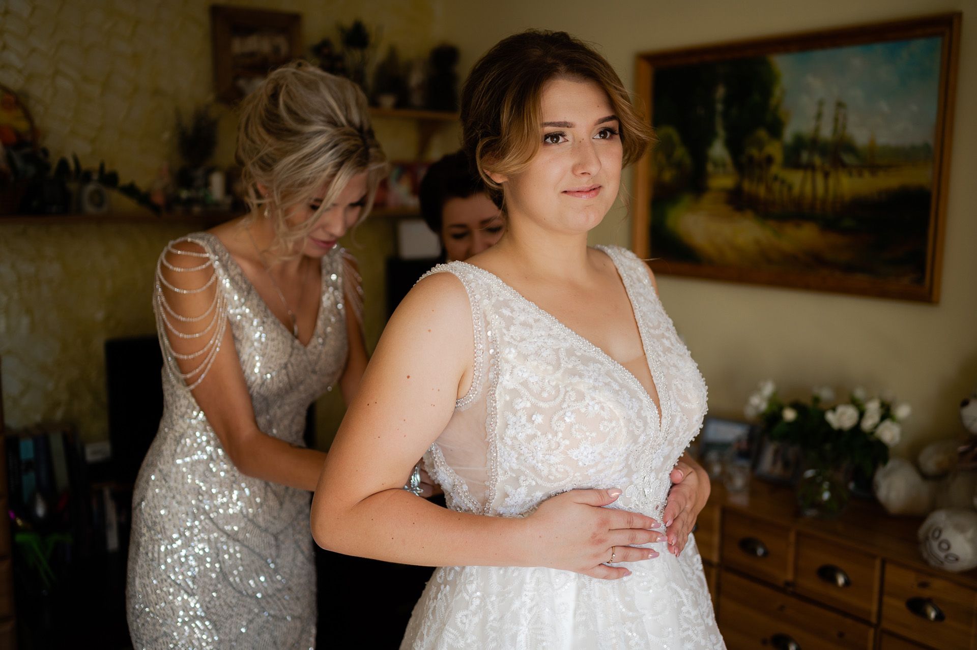 Matka pomagająca córce w założeniu białej koronkowej sukni ślubnej z perłami