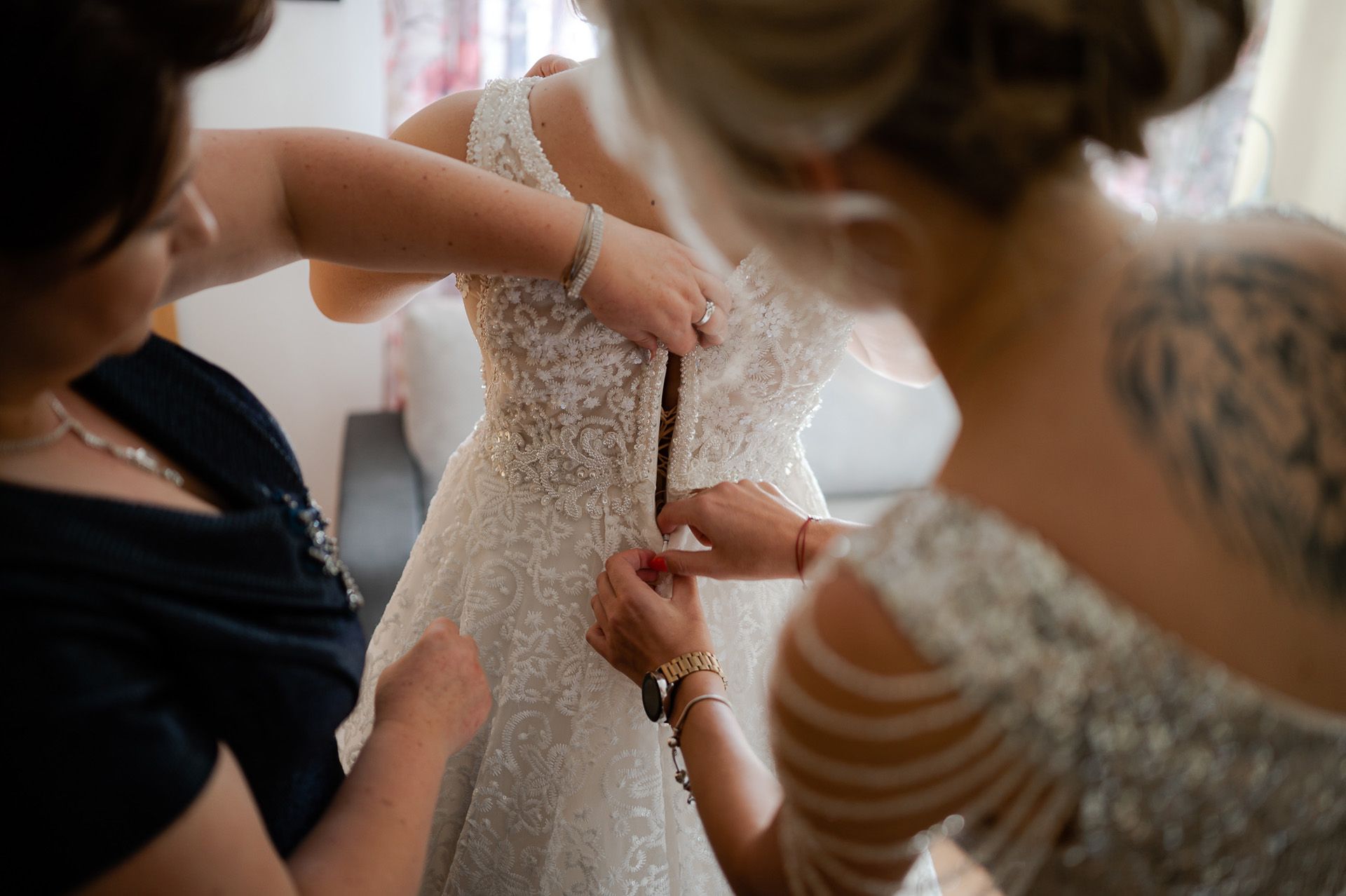 Zapinanie białej koronkowej sukni ślubnej przez druhny podczas przygotowań panny młodej