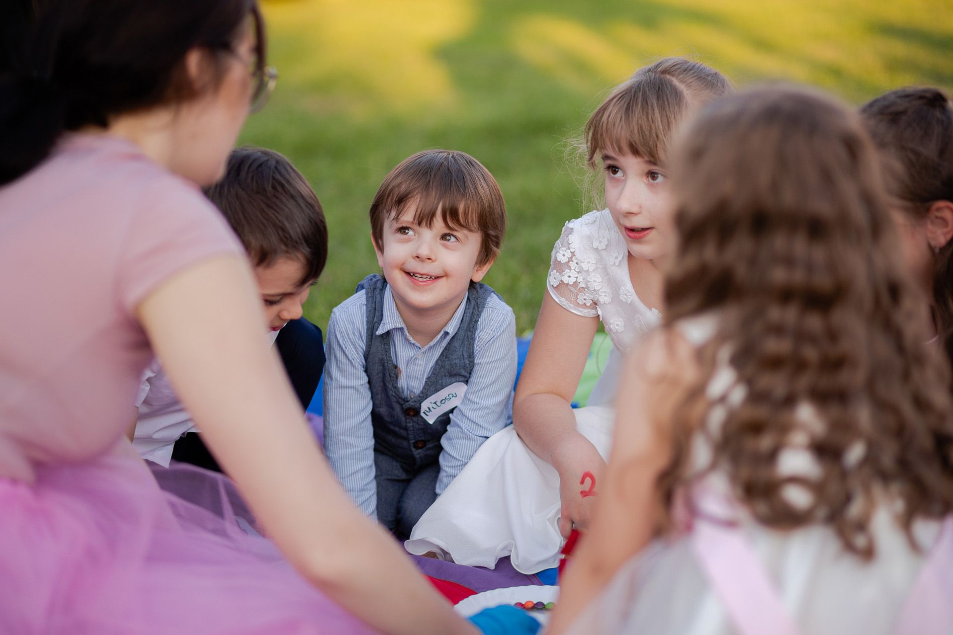Dzieci bawiące się na weselu na zewnątrz, chłopiec w kamizelce i dziewczynka w białej sukience, rodzinna atmosfera ślubu