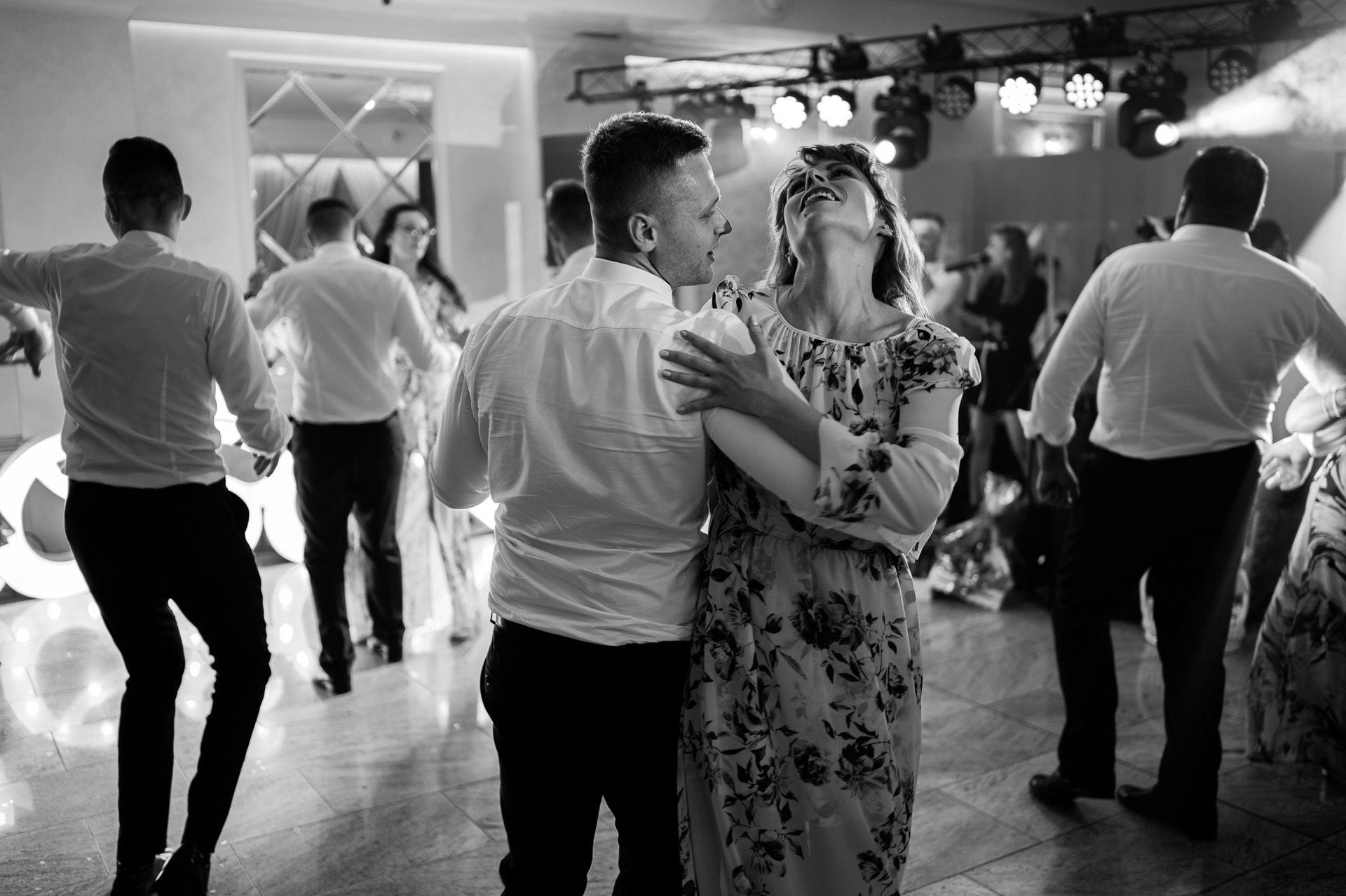 Goście weselni tańczą na parkiecie, para w czarno-białej fotografii ślubnej, kobieta śmieje się podczas tańca