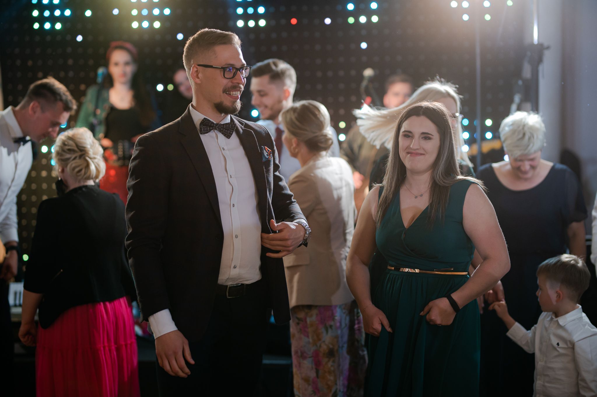 Goście weselni tańczą na parkiecie, mężczyzna w okularach z kobietą w zielonej sukience, wesele w eleganckich wnętrzach