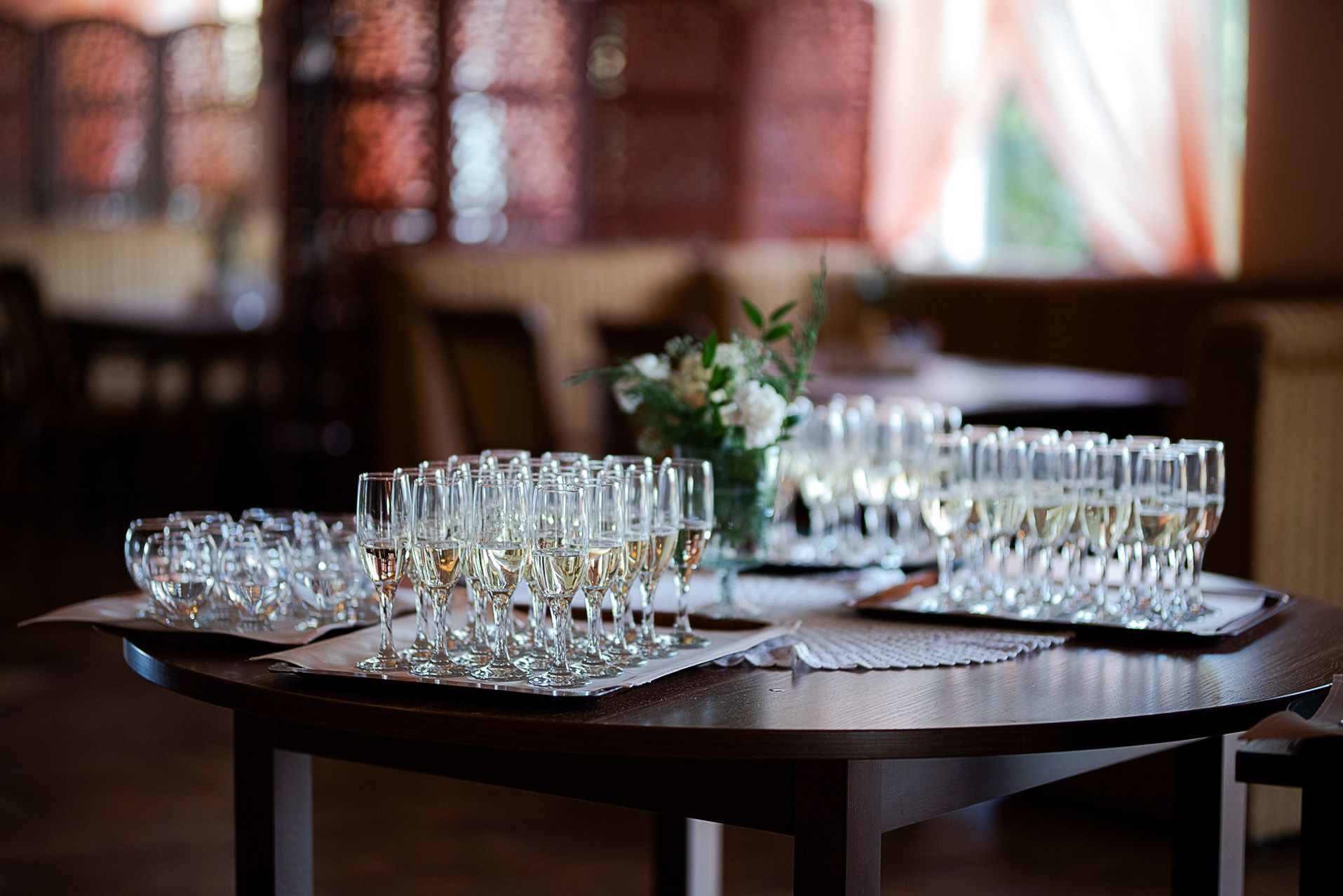 Eleganckie kieliszki szampana przygotowane na toast weselny, oprawa kwiatowa i lampki, przygotowania ślubne