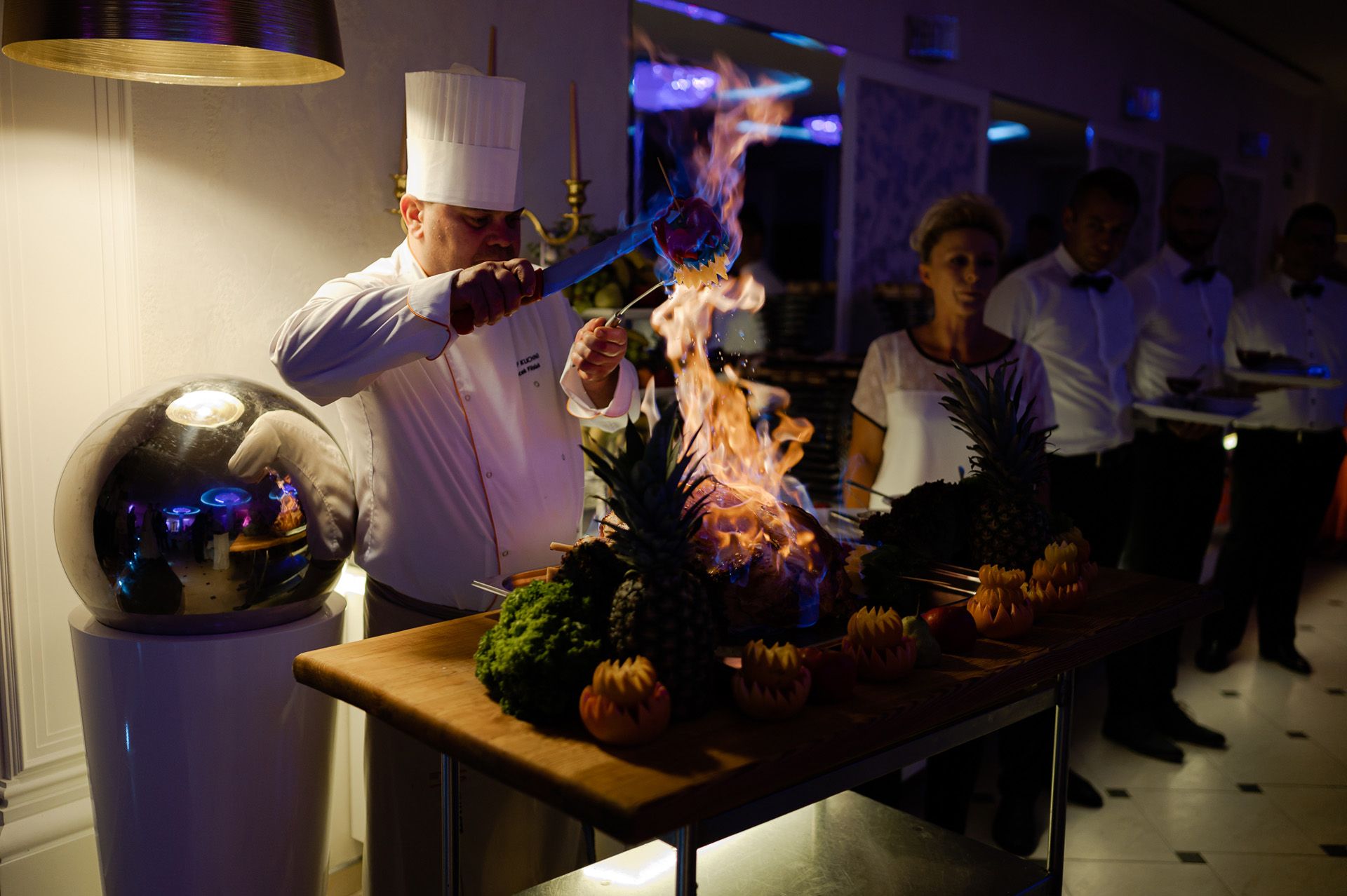 Szef kuchni w białym kapeluszu flambiruje potrawę podczas pokazu kulinarnego na weselu, spektakularny catering weselny