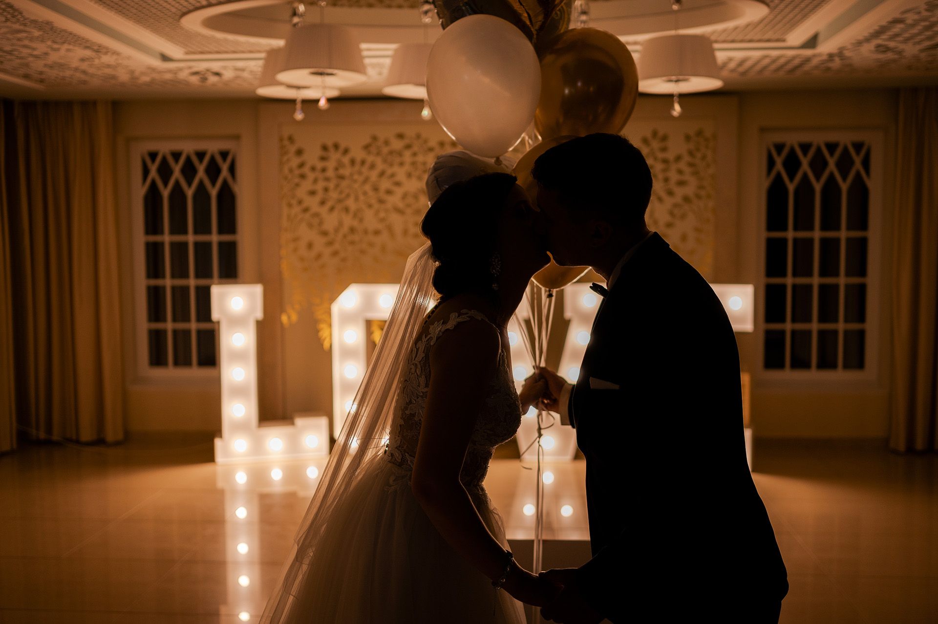 Romantyczny taniec pary młodej z lampkami w kształcie liter w tle, intymny moment ślubu w ciepłym świetle