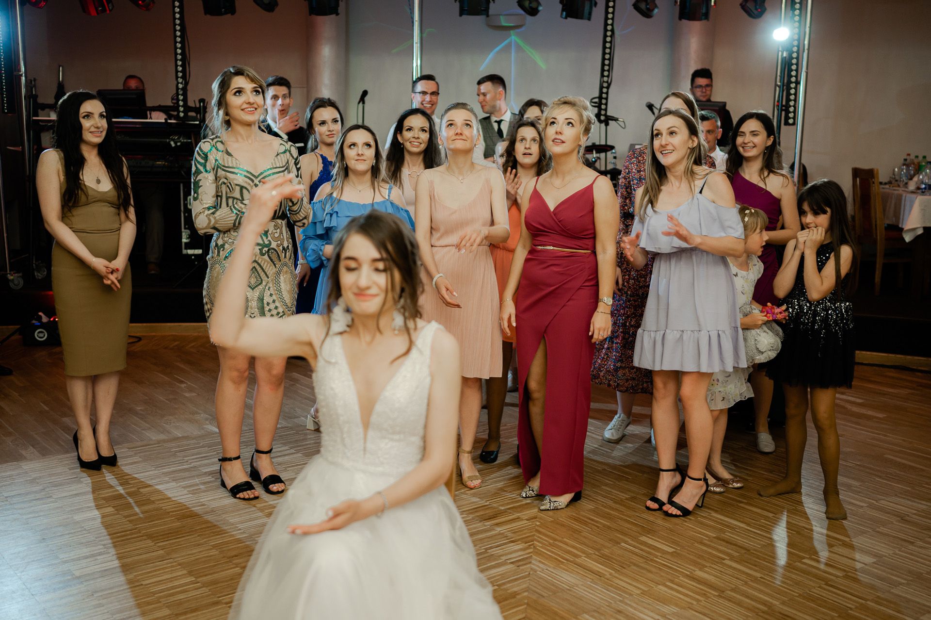 Panna młoda rzuca bukiet ślubny do grupy panien i druzhek w kolorowych sukienkach, tradycja weselna na parkiecie tanecznym