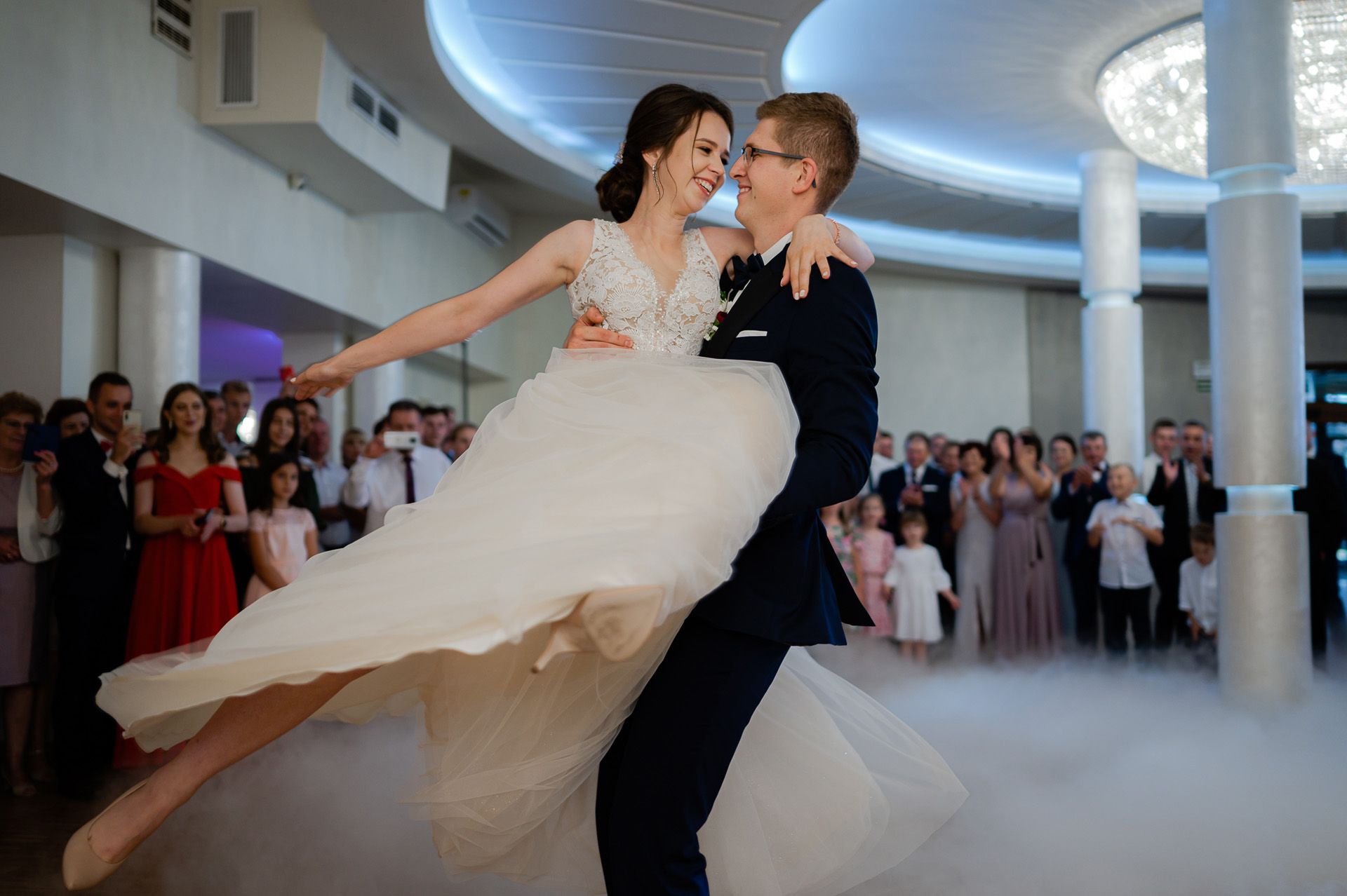 Para młoda tańczy w sali weselnej, wirująca suknia ślubna panny młodej, romantyczny taniec małżeński w otoczeniu gości