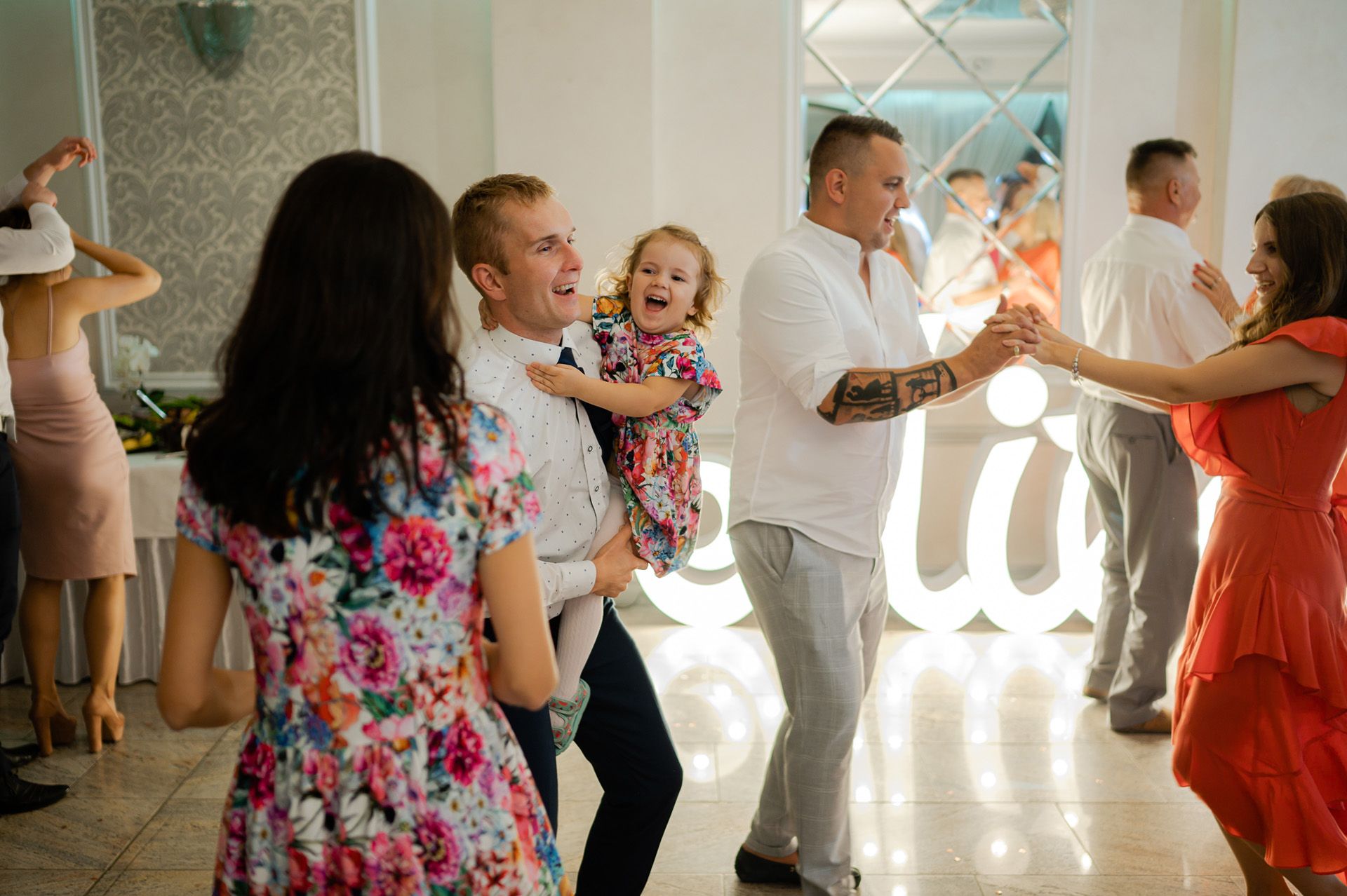 Rodzinny taniec na weselu z dziećmi, mężczyzna trzyma małą dziewczynkę, radosna atmosfera przyjęcia ślubnego