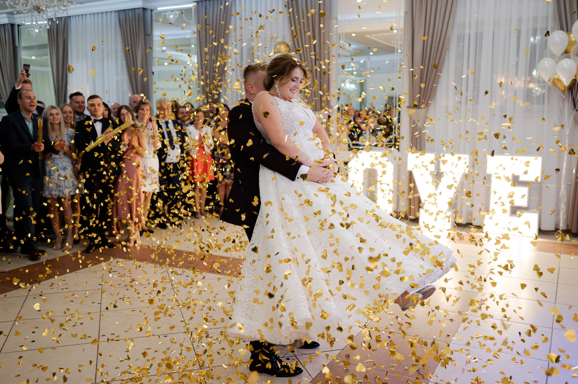 Para młoda tańczy pierwszy taniec w deszczu złotych konfetti, spektakularny efekt świetlny na weselu
